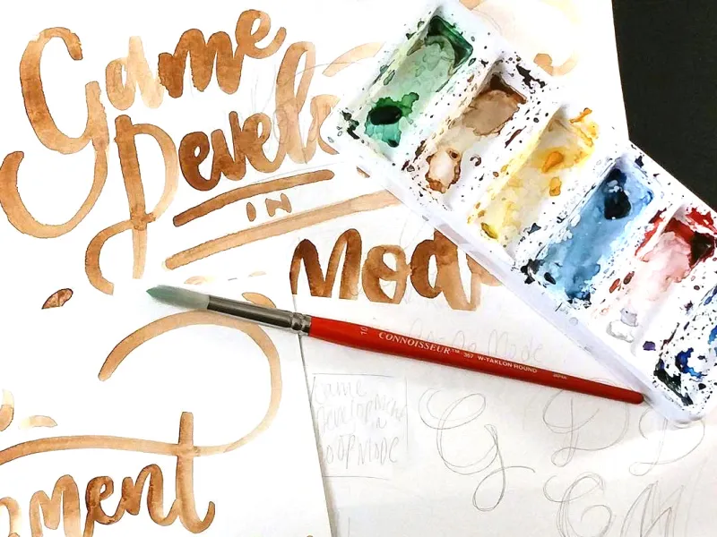 Watercolor paints and several pages of art showing the title process.